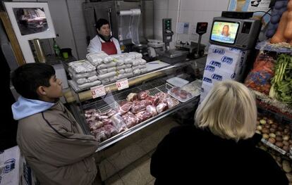Un empleado y dos clientes en una carnicería en Buenos Aires observan un discurso de Cristina Fernández.