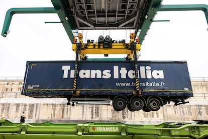 La gigantesca grúa verde acerca sus cuatro brazos de metal al primer camión cargado sobre el tren, lo engancha y lo eleva muchos metros. El operario explica: “Esta grúa se ha construido específicamente para este servicio, y hemos tenido que aprender a utilizarla. Es distinta de las de contenedores. Los cuatro brazos de la grúa enganchan el camión por cuatro puntos, lo sacan y lo dejan en el suelo".