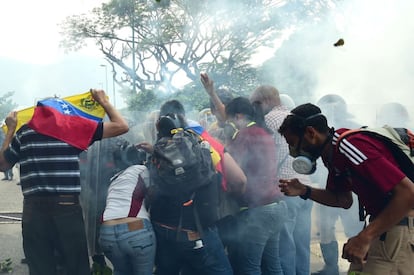 Un grupo de opositores del presidente del Gobierno se protegen de los agentes antidisturbios.