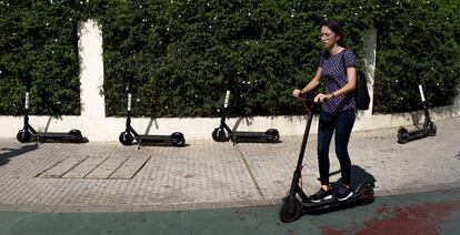 Una usuaria de patineta circula junto a cuatro unidades de uso compartido aparcadas en una acera de Sevilla