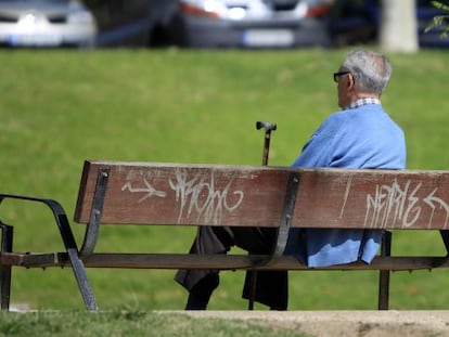 Un hombre sentado con su bast&oacute;n en un banco de un parque. 