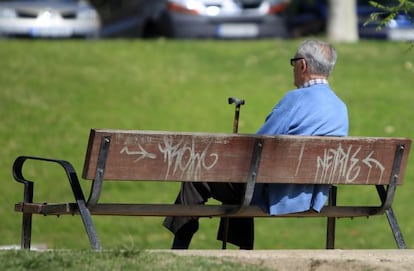 Un hombre sentado con su bast&oacute;n en un banco de un parque. 