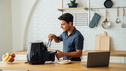 Un hombre cocinando con su freidora de aire en la cocina de su casa.