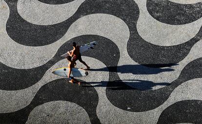 Dos hombres llevan tablas de surf en el paseo marítimo de Copacabana.