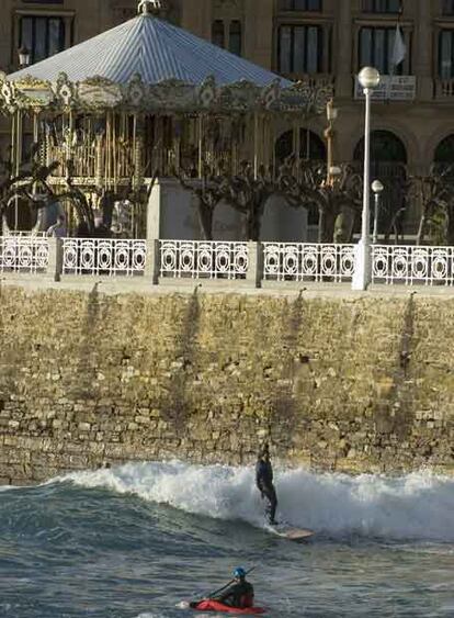 Un joven cabalga una ola con su tabla de surf en la playa de la Concha de San Sebastián, una zona muy protegida que necesita un fuerte temporal para la práctica de este deporte.