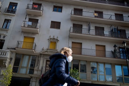 Una mujer pasa por delante de un edificio con varios pisos en venta y alquiler en Sevilla, este lunes.