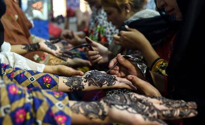 Varias esteticistas pakistaníes realizan tatuajes de henna a las clientas para la festividad del Eid al-Fitr, en un salón de belleza de Karachi (Pakistán).