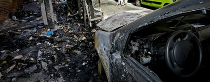 Un coche destrozado tras el incendio provocado de varios contenedores.