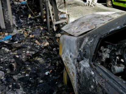 Un coche destrozado tras el incendio provocado de varios contenedores.