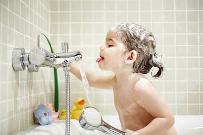 Bebé en la bañera intentando beber agua del grifo.