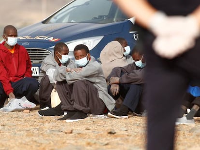 Un grupo de migrantes subsaharianos llegados en patera es vigilado por la policía nacional en la playa Aeroclub de la localidad de San Bartolome De Tirajana, en la isla de Gran Canaria, el 28 de agosto de 2020.  