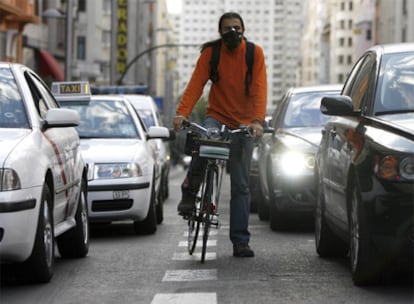 Un ciclista en la Gran Vía se tapa la boca con una mascarilla para no aspirar el humo de los coches.
