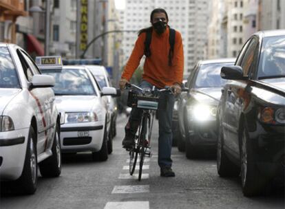 Un ciclista en la Gran Vía se tapa la boca con una mascarilla para no aspirar el humo de los coches.