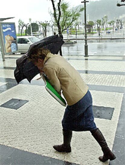 Una mujer trata de protegerse con un paraguas del fuerte viento y la lluvia en una calle de la capital donostiarra.