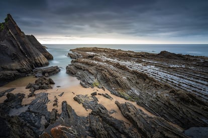 Saturraran, Mutriku (Gipuzkoa). Al principio fue el ‘flysch’ negro, esos vistosos estratos hojaldrados que testimonian la formación del golfo de Vizcaya. Se trata del ‘flysch’ más antiguo del Geoparque de la costa vasca, formado en un gran cañón submarino. La seña de identidad de Saturraran son los peñascos de Atxeku (es mejor fotografiarlos desde la carretera), pero también su típico caserío, algo no fácil de encontrar cerca de la rompiente. Tras el agradable paseo de medio kilómetro por este bello arenal, pisaremos detrás de los peñascos (mejor en bajamar) este ‘flysch’ sorprendente, junto a la escalera que conduce a una cala a mar abierto. Con los amonites gigantes hallados aquí se abrió el Centro de Interpretación Geológica, que luego habrá que visitar impepinablemente, sin olvidar la 'geoexcursión' en barco que zarpa del puerto motriqués.