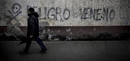 Un vecino cruza ante una pintada de advertencia sobre el lindano en las viviendas sociales de Torneiros, barrio de O Porri&ntilde;o.