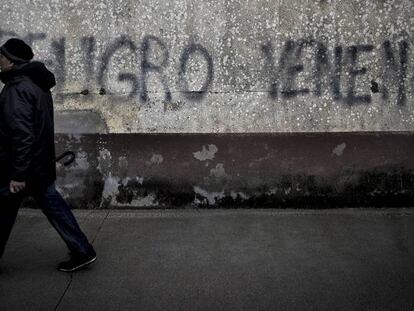 Un vecino cruza ante una pintada de advertencia sobre el lindano en las viviendas sociales de Torneiros, barrio de O Porri&ntilde;o.