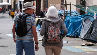 Dos turistas caminaban el lunes frente al campamento improvisado instalado por activistas que realizar una huelga de hambre para exigir al Gobierno de Canarias que paralice la construcción de dos proyectos urbanísticos en el sur de Tenerife, en la plaza de la Concepción en La Laguna.