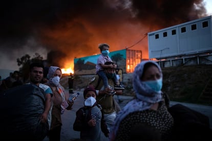 Un segundo incendio ha sido declarado este miércoles en el campo de refugiados de Moria, afectando a zonas que no habían sido alcanzadas por las llamas hasta ahora. En la imagen, varios refugiados abandonan el campo de Moria con algunas pertenencias. A sus espaldas, una gran columna de humo.