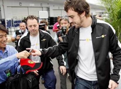 Alonso firma un autógrafo en una gorra de Ferrari.