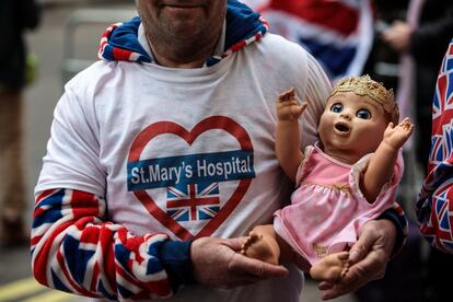 Uno de los asistentes al anuncio del nacimiento del tercer hijo de los duques de Cambridge lleva una muñeca con una corona y viste con ropa con la bandera británica. 