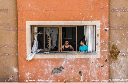 Dos hombres miran a través de una ventana dañada en Gaza.