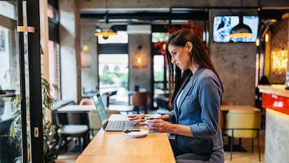 Una mujer trabajando en una mesa alta de una cafetería.
