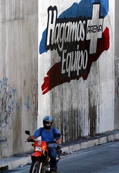 Un motorista pasa frente a un cartel electoral de Arena.