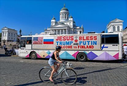 Una chica pasa con su bici por delante de un autobús decorado con el mensaje "Jesús bendiga a Trump y a Putin. Bienvenidos a Finlandia", en Helsinki (Finlandia).