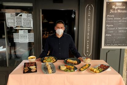 Cristian Morales ante un muestrario de los platos de su restaurante Panam en la calle Mayor de Alcalá de Henares. Por ahora, solo ofrece servicio a domicilio y para recoger en el local. En cuanto Madrid pase a la fase 1, plantará cinco mesas en la terraza, la mitad de las que suele.