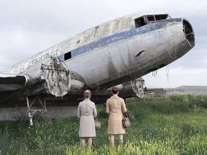 Duas mulheres em frente a uma fuselagem abandonada.