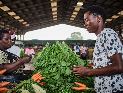 Un joven de la ciudad de Blantyre compra en el puesto de Ntanyula Loveness, una vendedora de verduras que tiene su negocio en el mercado desde 1993. Ella compra más caro que antes, pero no puede subir mucho sus precios porque si no pierde clientes, lo que la ha empobrecido aún más, explica.