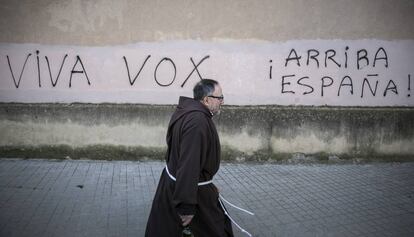 Un monje pasa ante unas pintadas favorables a Vox, en Barcelona.