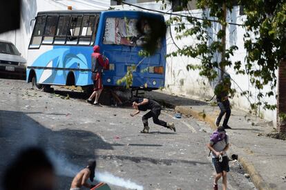 Um grupo de manifestantes se esconde atrás de um ônibus durante confronto com as forças de segurança venezuelanas.