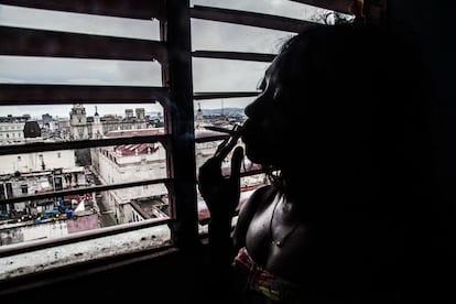 Una mujer se asoma en su habitación alquilada en Centro Habana. Cuando lleva clientes su casero le cobra una parte de la ganancia.