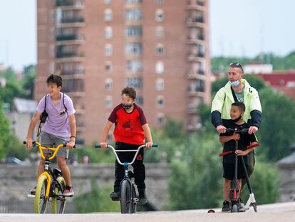 Dos niños montan en bicicleta y un señor en patinete en Madrid Río.