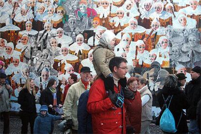 Turistas en el carnaval de Binche, en Bélgica, con los </i>Gilles,</i> los personajes característicos de la celebración, representados en la pared.