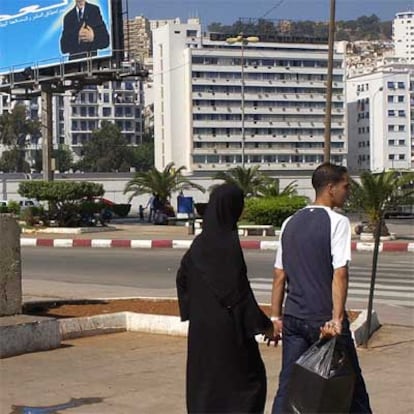 Una pareja de argelinos pasa ante un cartel electoral en Argel.