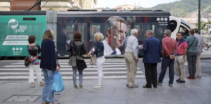 Ciudadanos observan el tranvía de Bilbao con publicidad electoral del PNV.