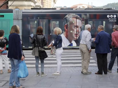 Ciudadanos observan el tranvía de Bilbao con publicidad electoral del PNV.