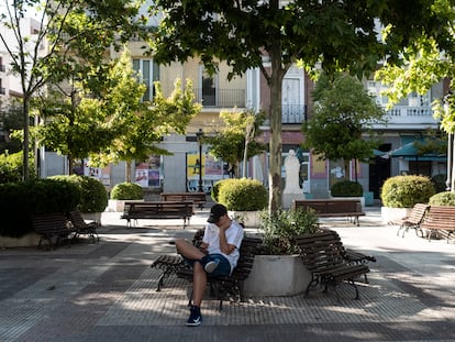 Un joven consulta su teléfono móvil en una plaza vacía del distrito de Chamberí (Madrid).