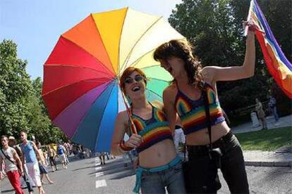Dos chicas se cubren del sol con un paraguas multicolor.