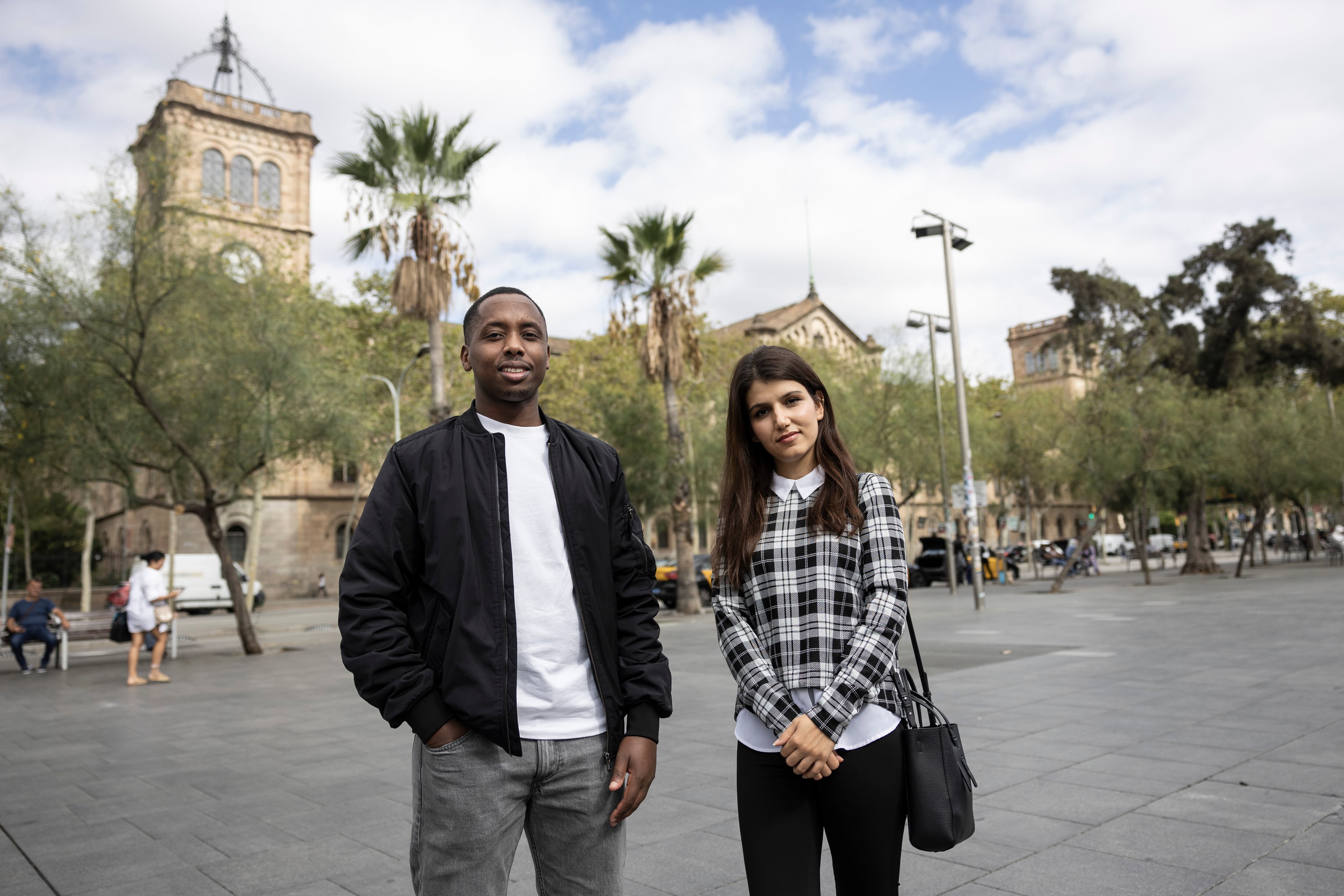 Bienvenu Iradukunda y Lina Fazly, dos refugiados con estudios superiores, en la plaza de la Universitat, con el edificio antiguo de la Universidad de Barcelona al fondo.