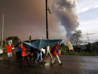 Varios ciudadanos se cubren con una manta mientras evacuan la ciudad de Tagaytay. Al fondo, la columna de humo del volcán Taal.