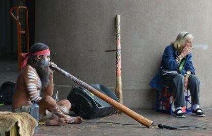 Una anciana fuma un cigarrillo mientras un hombre toca el 'didgeridoo' en Circular Quay, en Sydney (Australia).