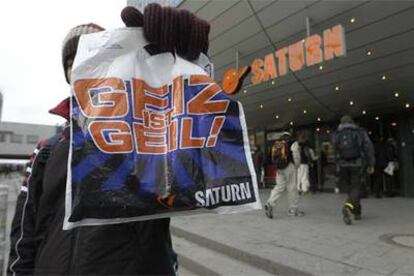 Un joven muestra una bolsa con el eslogan <i>¡Geiz ist geil!</i> junto a una conocida tienda de Berlín.