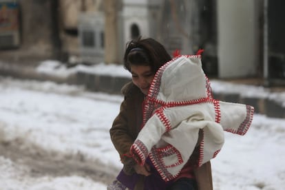 Un niña (con su hermana pequeña en brazos) juega en la nieve a pesar de las heladas temperaturas.