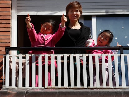 Wei Chen y sus hijas saludan desde el balcón de su piso de Barcelona, donde llevan una semana confinadas.