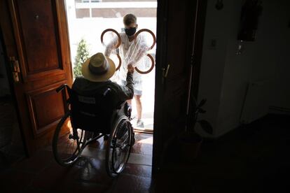Ramiro Pisani toma de la mano de su abuelo Pedro Aberastegui a través de una funda plástica desde el exterior de una residencia de ancianos en Argentina.