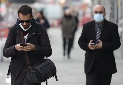 Dos hombres pasean por Madrid con y sin mascarilla.